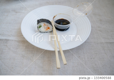 sushi roll with chopsticks and wasabi sauce in a plastic container on a white plate. sushi roll with chopsticks and wasabi sauce in a plastic container on a white plate. 133400588