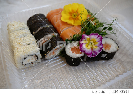 Mix of sushi rolls with salmon, avocado, smoked eel, in a plastic food delivery box. 133400591