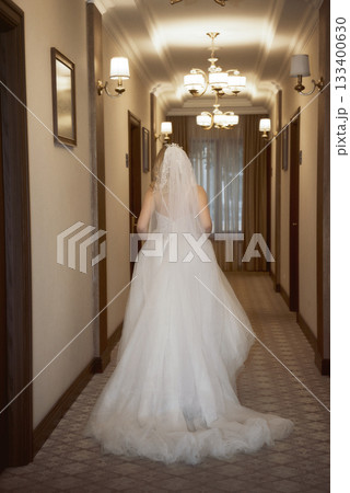 beautiful blonde bride with veil in hotel hallway in fashionable dress, back view. 133400630
