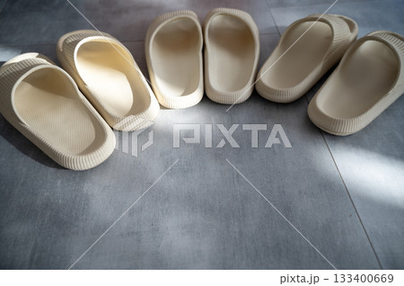 Three pairs of beige rubber slippers stand on a gray granite floor 133400669
