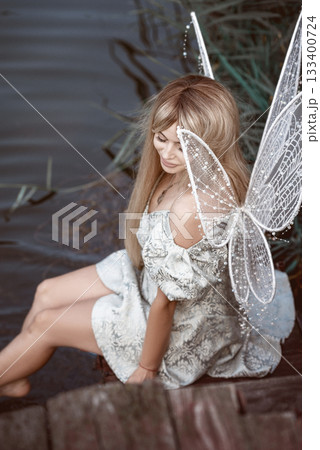 cute blonde girl in fairy costume with wings. girl sitting on pier near river 133400724