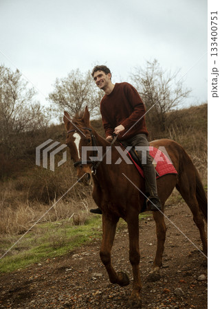 A man in a brown sweater rides uphill on a horse across a field A man in a brown sweater rides uphill on a horse across a field 133400751