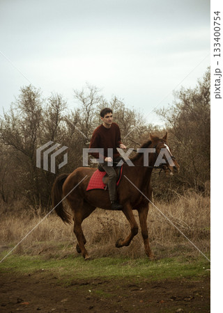 A man in a brown sweater rides uphill on a horse across a field A man in a brown sweater rides uphill on a horse across a field 133400754