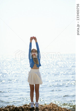Beautiful blonde girl stands on a sandy beach in sunny weather. Sunset 133400756