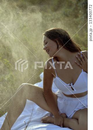 Water drops falling on young girl in beachwear on grass in field in rays of sunset sun. Water drops falling on young girl in beachwear on grass in field in rays of sunset sun. 133400772