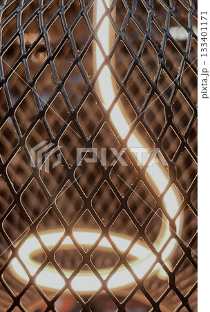 Close-up of a warm glowing LED filament light bulb inside a diamond metal mesh cage 133401171