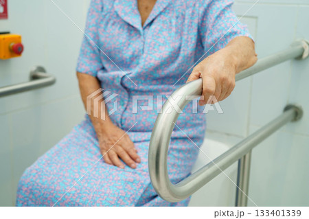Asian elderly woman patient use toilet support rail in bathroom. 133401339