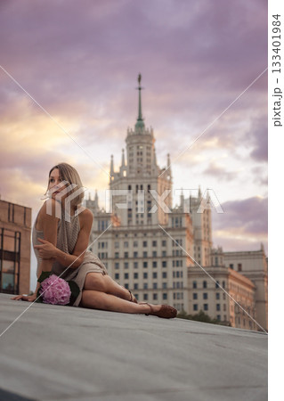 A woman sits on the Tessinsky Bridge with the Kotelnicheskaya Embankment Building rising behind her at sunset A woman sits on the Tessinsky Bridge with the Kotelnicheskaya Embankment Building rising behind her at sunset 133401984
