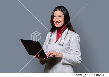 Portrait of female doctor with laptop on gray background 133402618