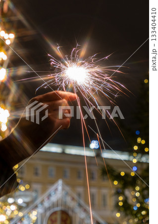 hand holding sparkler in front of Christmas tree. picture shows festive and joyful mood. 133404410