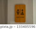 Wooden restroom sign with male and female symbols mounted on a clean white wall 133405596