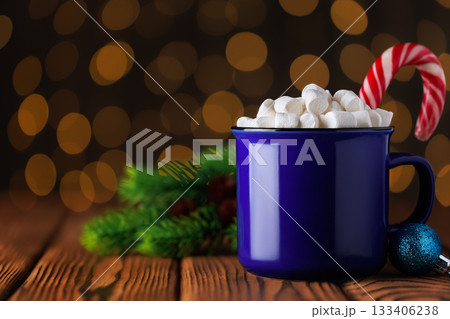 Blue cup of hot cocoa with marshmallows and candy cane on wooden table against background of bokeh glowing garland lights Blue cup of hot cocoa with marshmallows and candy cane on wooden table against background of bokeh glowing garland lights 133406238