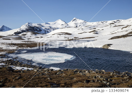 Winter landscape with melting ice and snow-capped mountains in a clear blue sky Winter landscape with melting ice and snow-capped mountains in a clear blue sky 133409074