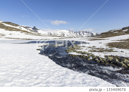 Snowy landscape of Leirvassbu in Leirdalen showcasing a flowing river in Jotunheimen National Park under a clear blue sky 133409078