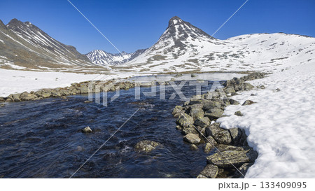 Scenic winter view of Leirvassbu with snow-covered mountains and a flowing river in Jotunheimen National Park 133409095