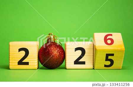 2026 New Year symbol. Businessman turns wooden cube and changes Year 2025 to 2026. Beautiful green background with christmas ball. Copy space. Business and 2026 happy new year concept 133411256