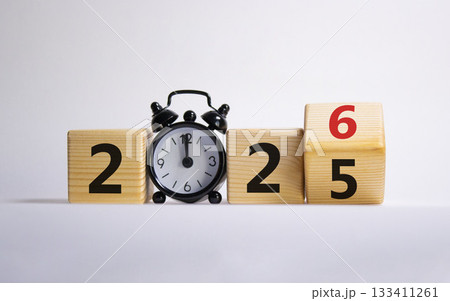 2026 New Year symbol. Businessman turns wooden cube and changes Year 2025 to 2026. Beautiful white background with Alarm clock. Copy space. Business and 2026 happy new year concept 133411261