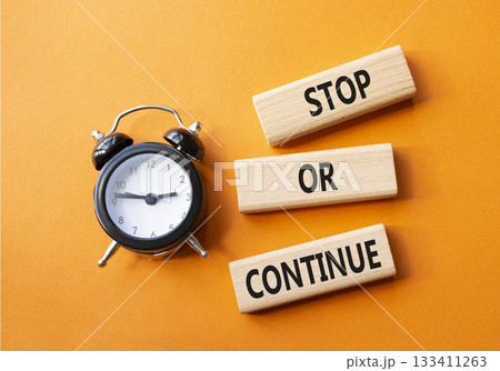 Stop or Continue symbol. Concept words Stop or Continue on wooden blocks. Beautiful orange background with alarm clock. Business concept and Stop or Continue. Copy space. 133411263