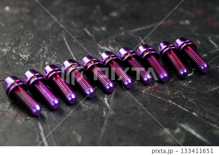 A series of titanium pink hexagon head screws on a black textured background close-up 133411651
