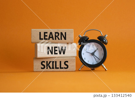 Learn new skills symbol. Concept words Learn new skills on wooden blocks. Beautiful orange background with alarm clock. Business and Learn new skills concept. Copy space. 133412540