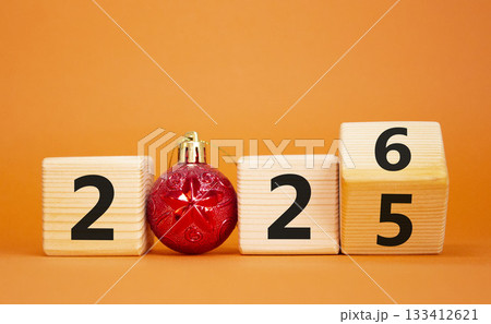 2026 New Year symbol. Businessman turns wooden cube and changes Year 2025 to 2026. Beautiful orange background with christmas ball. Copy space. Business and 2026 happy new year concept 133412621
