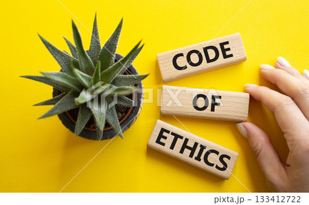 Code of ethics symbol. Concept words Code of ethics on wooden blocks. Businessman hand. Beautiful yellow background with succulent plant. Business and Code of ethics concept. Copy space. 133412722