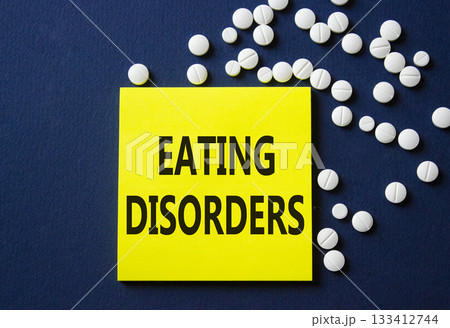 Eating Disorders symbol. Concept word Eating Disorders on yellow note. Beautiful deep blue background with pills. Medicine and Eating Disorders concept. Copy space 133412744