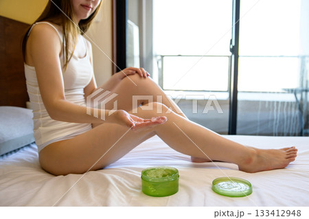ベッドでボディジェルを手に取る下着姿の若いスレンダーな女性 フットケア トリミングアップ ベッドでボディジェルを手に取る下着姿の若いスレンダーな女性 フットケア トリミングアップ 133412948