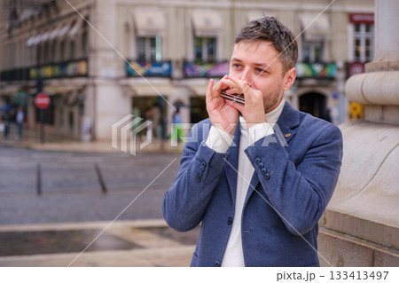 Man musician in a blue blazer and white sweater playing blues on a harmonica with eyes closed, standing outdoors in Lisbon city street, Portugal 133413497
