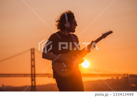Hipster street musician in black playing electric guitar in street outdoors on sunset with lens flare and light leak Hipster street musician in black playing electric guitar in street outdoors on sunset with lens flare and light leak 133413499