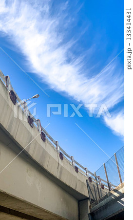The bright blue sky and wispy clouds contrast with the concrete structure of the bridge, creating an interesting visual The bright blue sky and wispy clouds contrast with the concrete structure of the bridge, creating an interesting visual 133414431