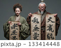 Two individuals in traditional attire showcase ancient calligraphy scrolls. 133414448