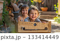 Two joyful children play in a cardboard box, enjoying their imaginative adventure outdoors. 133414449