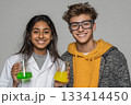Two students smiling while holding colorful beakers in a lab setting. 133414450