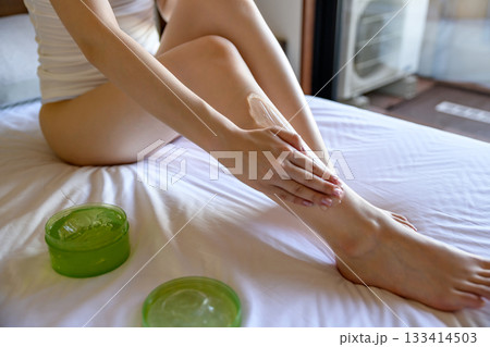ベッドでボディジェルを脚に塗る下着姿の若いスレンダーな女性　スキンケア　フットケア　昼カラー 133414503