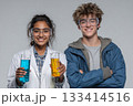 Two young scientists proudly holding colorful liquid samples in a laboratory. 133414516