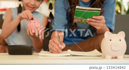 Teaching Financial Skills. Mother and daughter saving money with piggy banks. 133414842