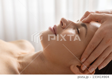 Closeup side view of young woman receiving gentle face massage at spa 133414904