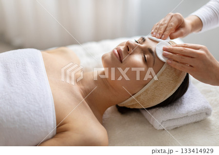 Therapist cleansing forehead of young beautiful woman with cotton pads. Therapist cleansing forehead of young beautiful woman with cotton pads. 133414929