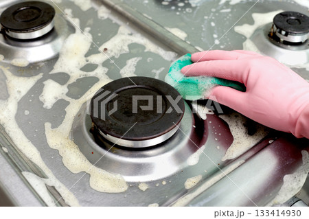 Hand in pink glove cleaning a greasy gas stove with sponge and foam. Close-up of household kitchen cleaning process. 133414930