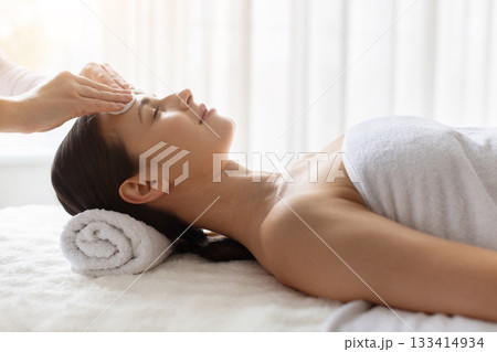 Young woman receiving gentle forehead cleansing at spa, enjoying skincare 133414934