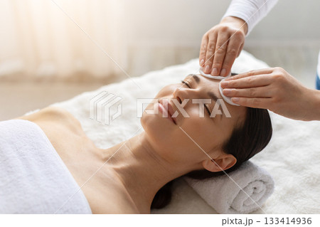 Therapist cleaning forehead of young woman with cotton pads during spa session Therapist cleaning forehead of young woman with cotton pads during spa session 133414936