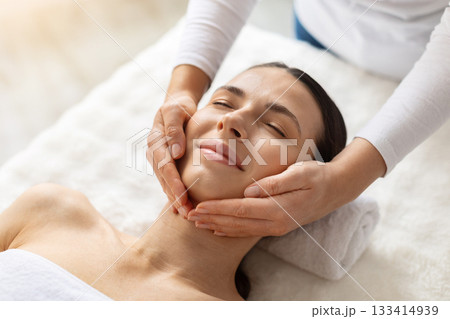 Young female enjoying relaxing facial massage at spa, eyes closed in comfort 133414939