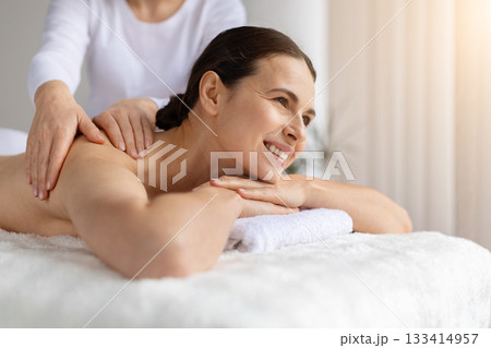 Young woman receiving relaxing shoulder massage, smiling slightly Young woman receiving relaxing shoulder massage, smiling slightly 133414957