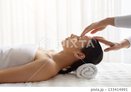 Young female relaxing during calming spa treatment as therapist gently touching forehead Young female relaxing during calming spa treatment as therapist gently touching forehead 133414991