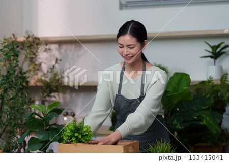 Sustainability. Smiling woman arranging potted plants in a cozy indoor garden. Sustainability. Smiling woman arranging potted plants in a cozy indoor garden. 133415041