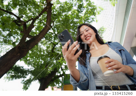 Smiling woman with coffee and smartphone in urban setting 133415260