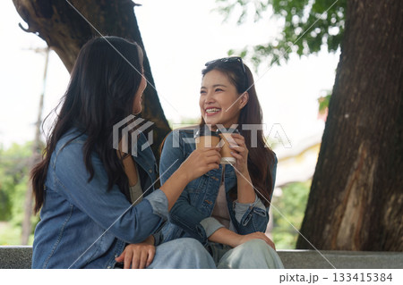 Coffee and Connection. Two young women enjoying coffee and laughter together in a park. 133415384