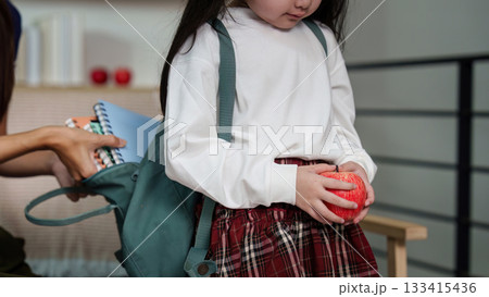 Mother assisting daughter with school essentials, including an apple. 133415436