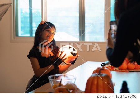 Halloween Spirit. Young girl posing with a carved pumpkin while mother takes a photo. Halloween Spirit. Young girl posing with a carved pumpkin while mother takes a photo. 133415686